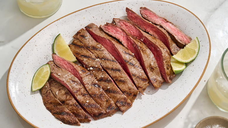 Flank steak sliced on a platter with lime wedges