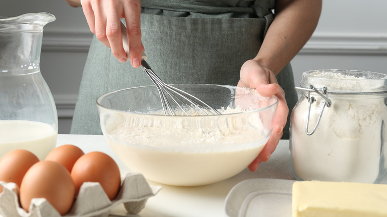 Person whisking flour, butter, and milk together in a large glass bowl