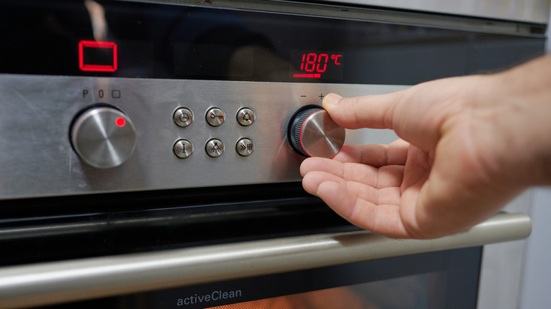Hand turning the knob of an oven to set the temperature