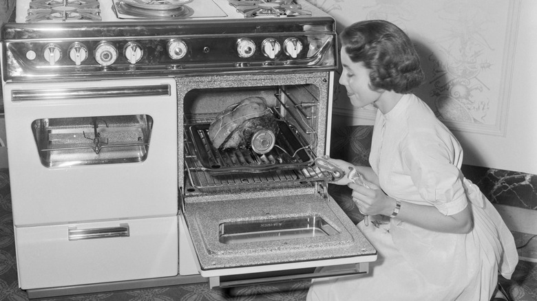 1950s picture of woman cooking meat in oven