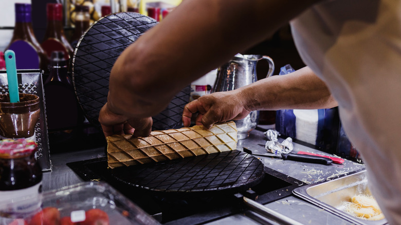 A close-up of a woman's hands rolling a marquesita on a crepe press