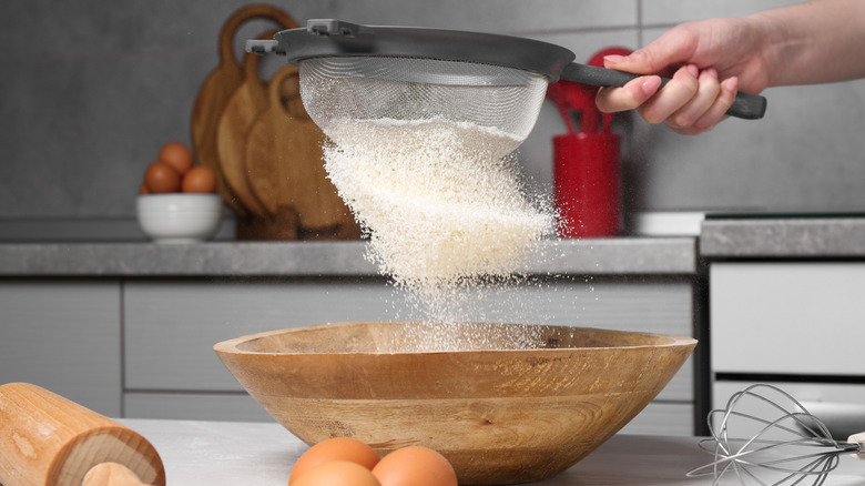 A woman sifting flour through a sieve while baking