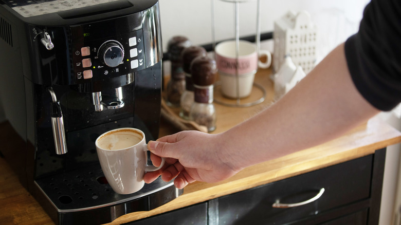 a hand holding a coffee cup beneath a home espresso machine