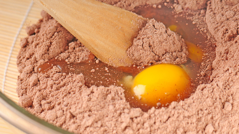 Chocolate cake mix in mixing bowl with egg and wooden spoon