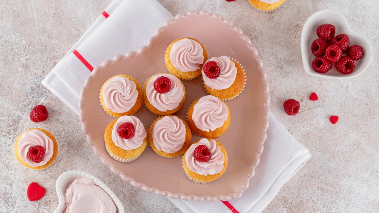 Cupcakes topped with fresh raspberries and pink frosting, arranged on heart-shaped plate