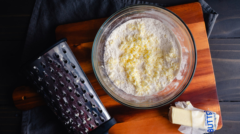 Grating frozen butter into flour mixture in glass mixing bowl