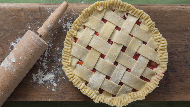 Unbaked, lattice-topped fruit pie on wooden board with rolling pin