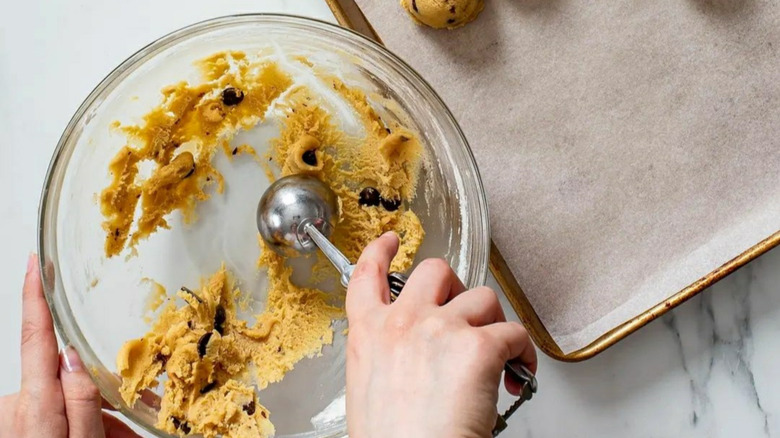 Scooping cookie dough from bowl onto baking sheet with ice cream scoop