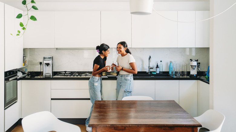 Two women laughing in a white modern kitchen with smooth surfaces
