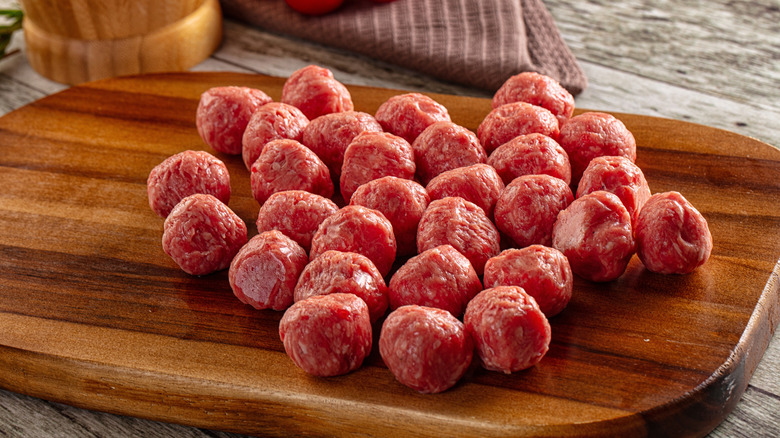 Cutting board covered in a number of raw meatballs