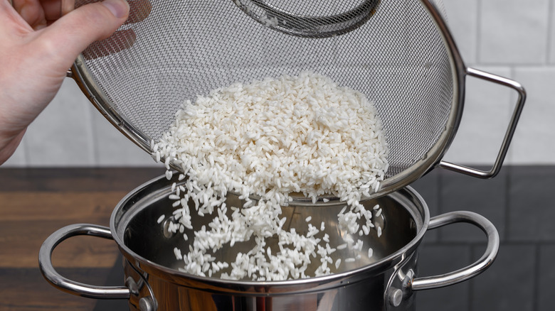 A person adding rinsed and drained white rice to a pot to cook
