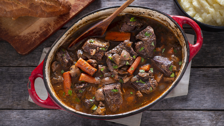 beef bourguignon in red enamel pot with wooden spoon