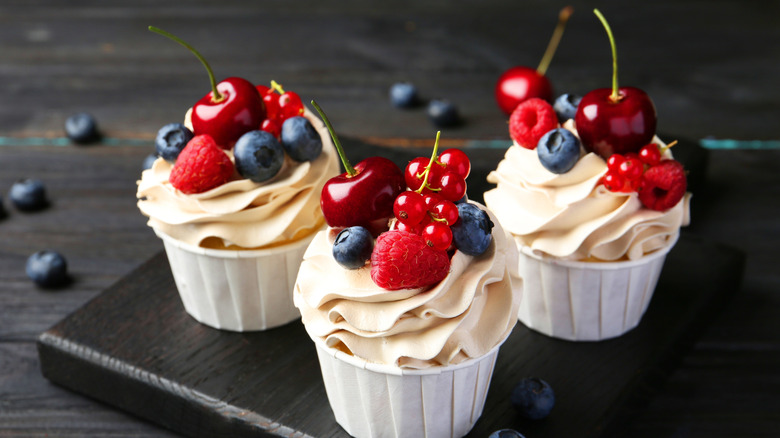 Three frosted cupcakes with fresh cherries, raspberries, bluebarries, and cranberries on top
