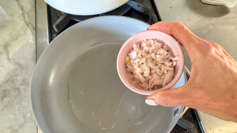 hand adding shallots to pan