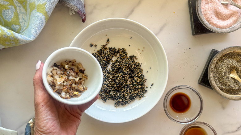 hand adding shallots to bowl with sesame seeds
