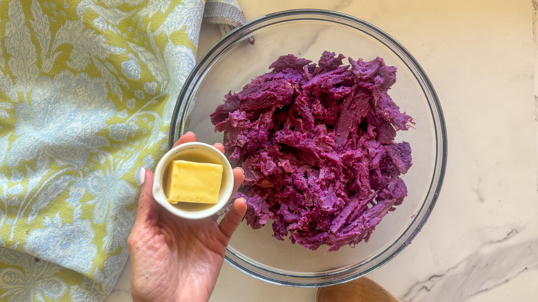 hand adding butter to bowl with purple potatoes