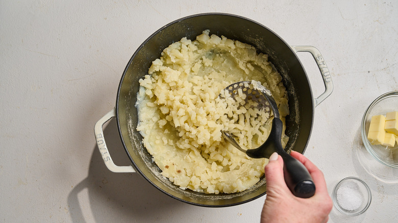 mashed potatoes in a pot with a potato masher