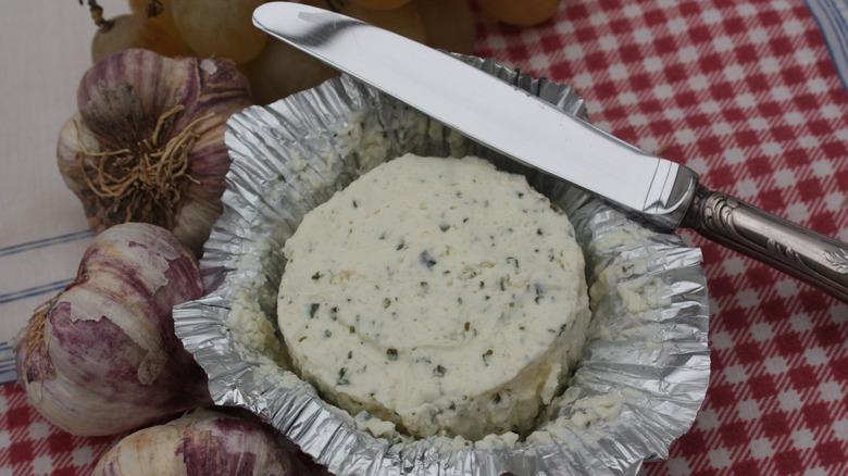 Boursin cheese with garlic cloves and a knife on a checked cloth