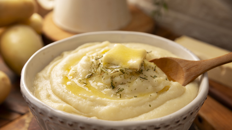 Mashed potatoes with butter in a bowl on a wooden cutting board