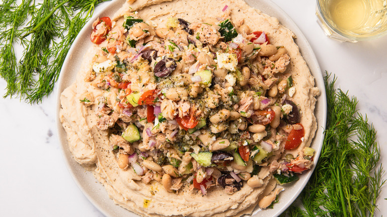 White bean and tuna salad with dill around beside a glass of wine