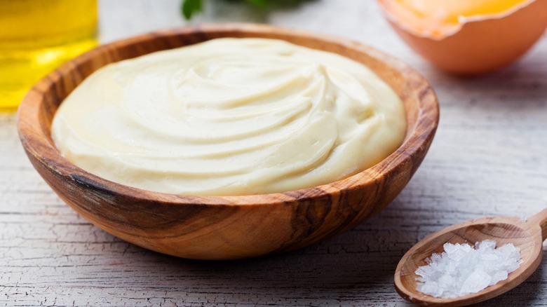 Wooden bowl of mayonnaise next to a spoon of salt