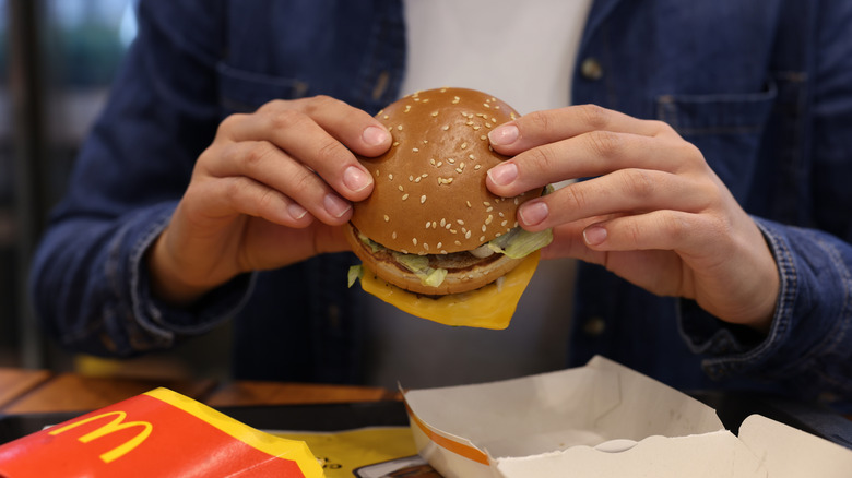 Person in white shirt and jean jacket holding a Big Mac in their hands