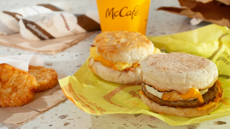 McDonald's sausage and egg McMuffin next to a biscuit, with hash browns on the side and a McCafe coffee in the background
