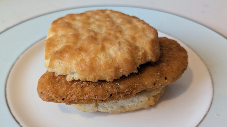 A fluffy white biscuit is sliced in half and served around a single golden fried piece of chicken, sitting on a blue and white plate