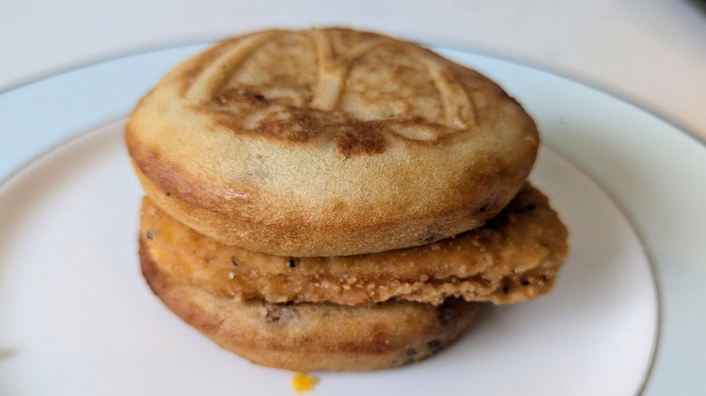 A blue and white plate features a McGriddle sandwich with the iconic McDonald's "M" arch logo visible on the top bun. In between the maple-syrup filled patties is a single golden-fried chicken breast