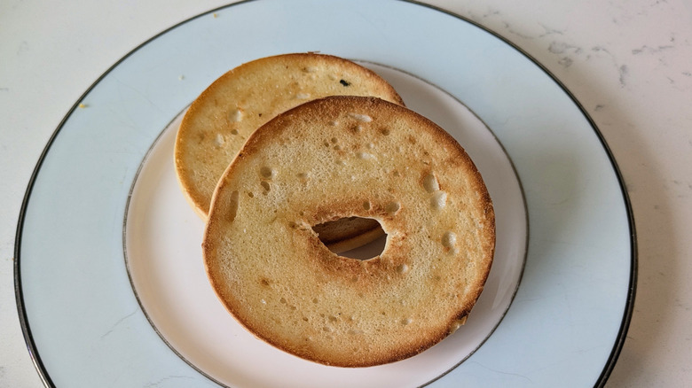 A single bagel is sliced in half, toasted, and stacked slightly on top of one another on a blue and white plate