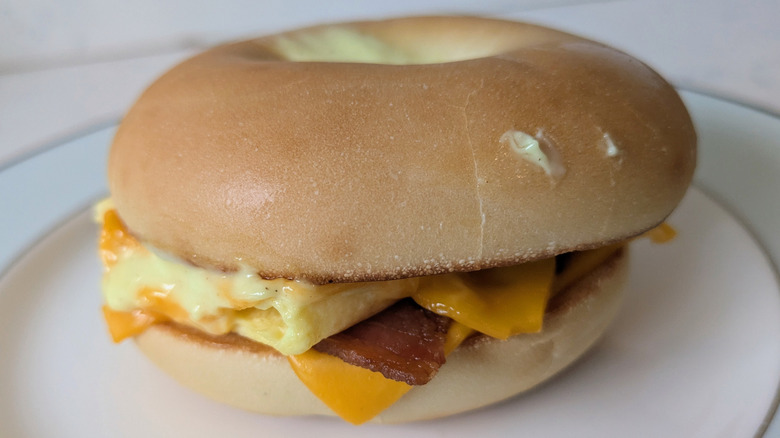 A bagel sliced in half is toasted and topped with cheese, bacon, fluffy eggs, and a creamy yellow-white sauce
