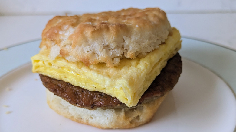 A fluffy biscuit is sliced in half and topped with a fluffy egg patty and a sausage patty on a blue and white plate