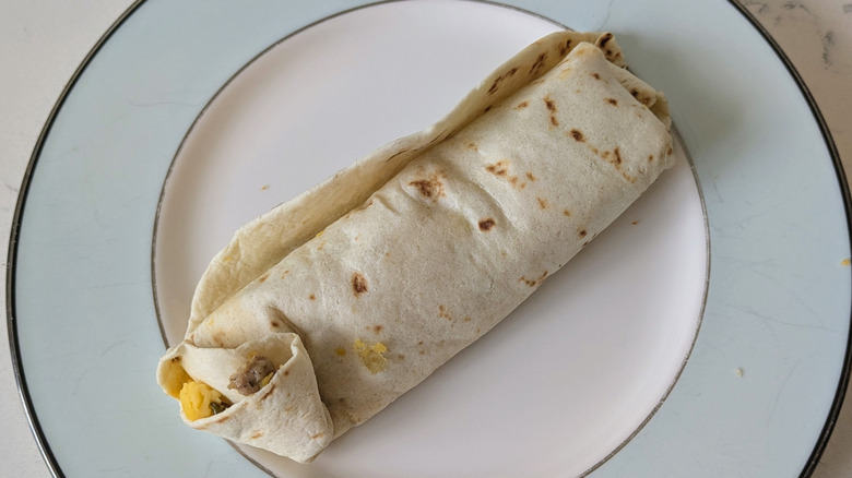 A flour tortilla is wrapped around sausage crumbles, a Southwestern pepper vegetable mix, and scrambled eggs, on a blue and white plate
