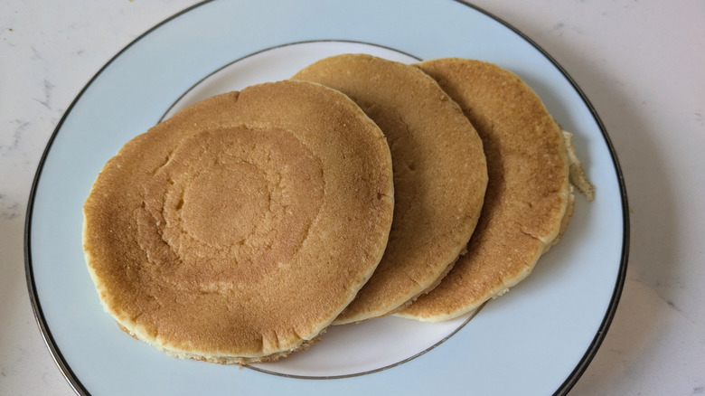 Three large and fluffy, golden brown pancakes are stacked on a white and blue plate