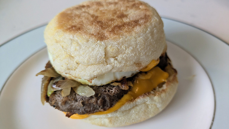 An English muffin is toasted and sliced in half, topped with a steak patty, grilled white onions, and a slice of cheddar cheese on a blue and white plate