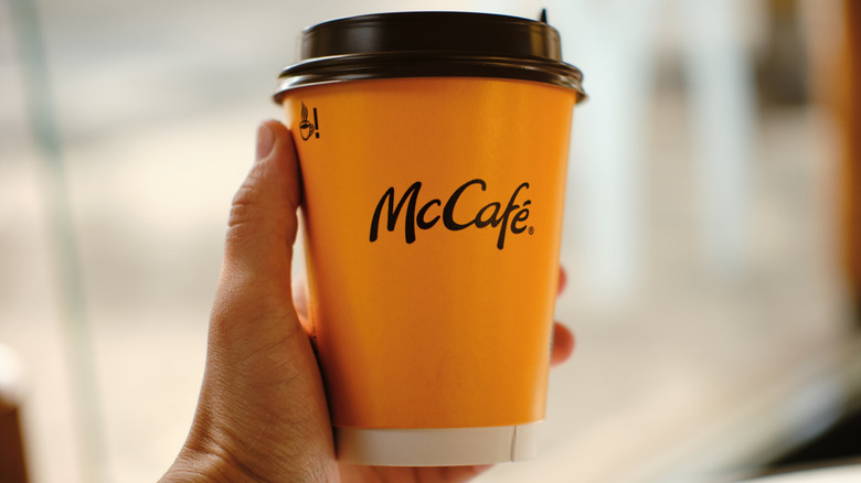 A hand holding up a yellow McCafé-branded paper cup.