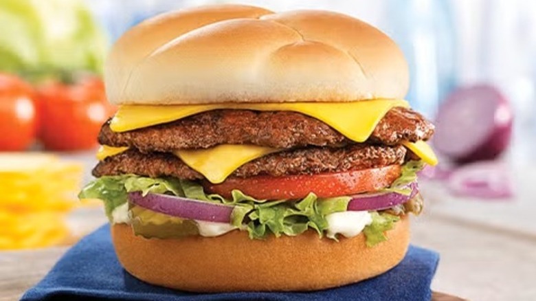 A double cheeseburger topped with lettuce, red onion, mayo, and tomato, sitting on a blue towel