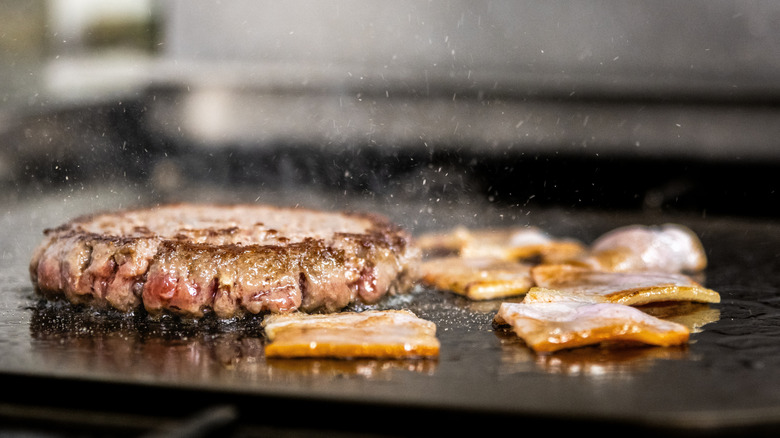 Angus beef and bacon sizzling on a griddle