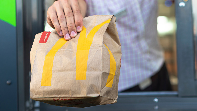 A McDonald's employee holds out a branded paper bag of food from a drive thru service window