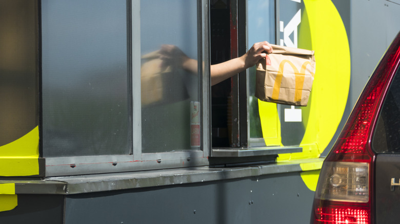 An attendant hands over food at a Mc Donald's drive-thru window