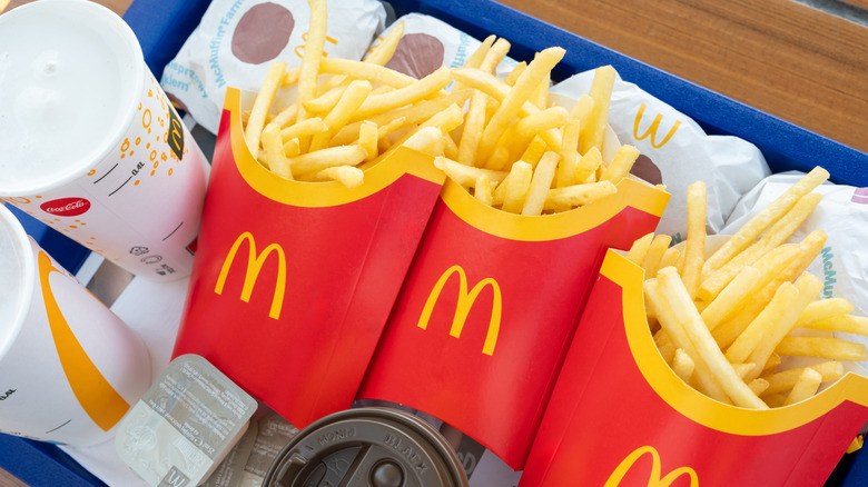 Three servings of McDonald's fries on a tray with drinks and burgers