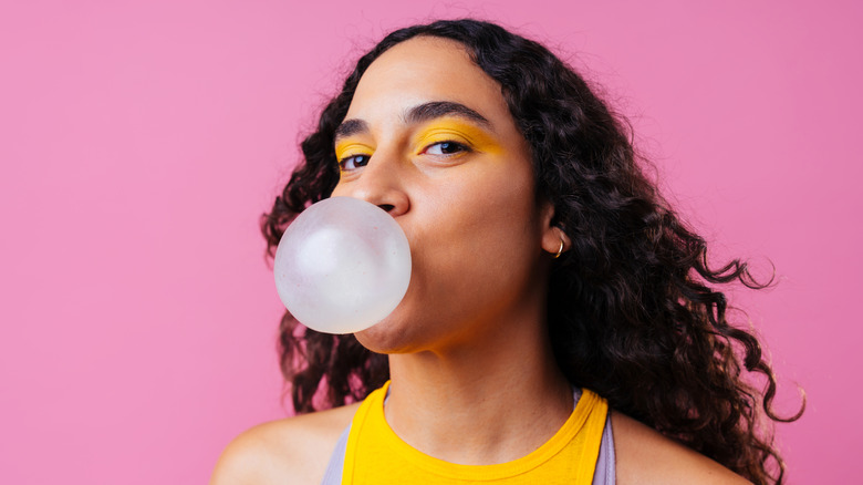 A woman blowing a gum bubble against pink background
