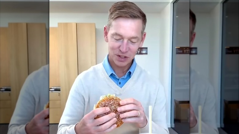 Chris Kempczinski looking curiously at the Big Arch burger he is holding in his hands