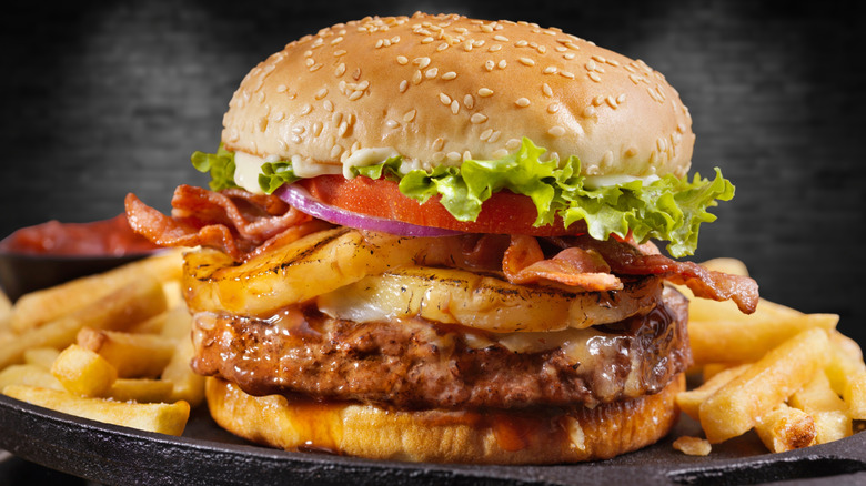 Burger with pineapple and bacon on a plate with fries