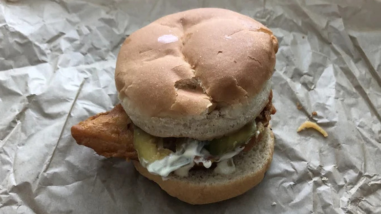 A fish sandwich from Long John Silver's with tartar sauce and pickles, sitting on crumpled paper