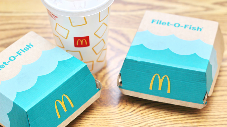 Two branded cardboard containers from McDonald's marked "Filet-O-Fish", alongside a McDonald's Styrofoam cup, sitting on a wooden table