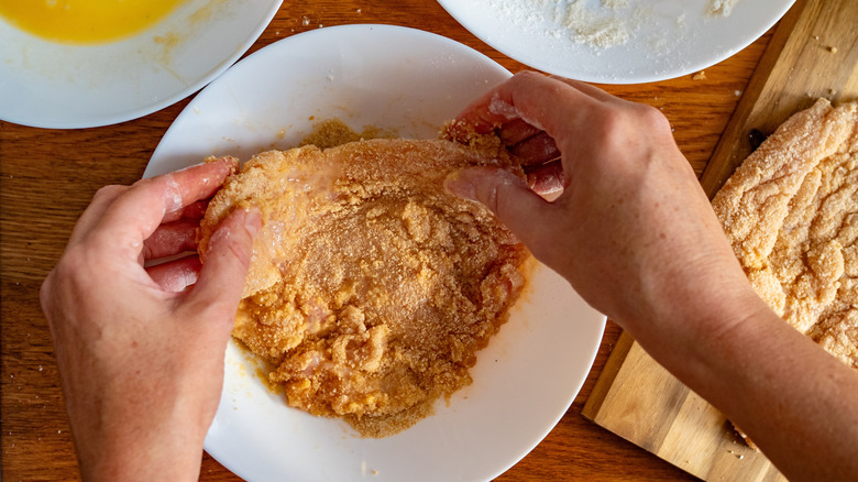 Someone hand breading chicken cutlets, with plates of egg and flour visible just out of frame