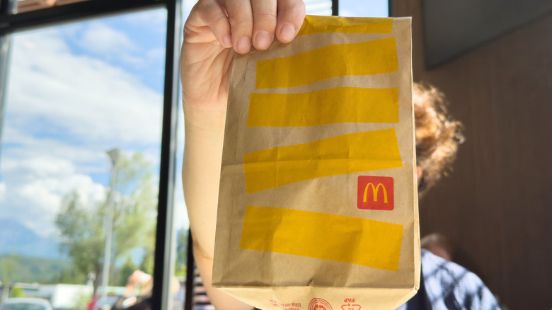 McDonald's employee holding a takeout bag of food at a drive-thru window
