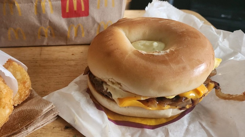 A McDonald's egg and steak breakfast bagel next to a hash brown in a paper wrapper