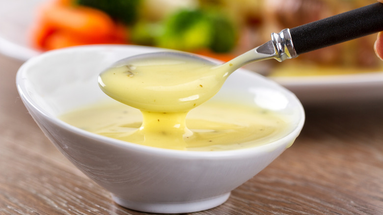 Close-up of spoon being dipped a spoon into a white bowl of béarnaise sauce